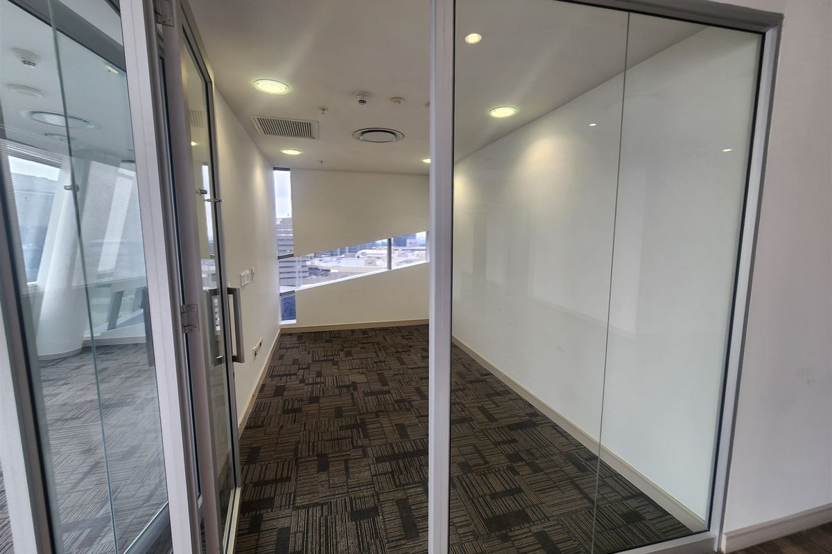 A modern, empty office space featuring glass partition walls, recessed lighting, and patterned carpet tiles, offering a clean and professional environment.