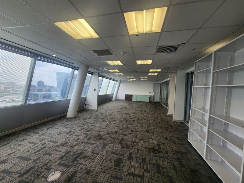 Spacious open-plan office area featuring floor-to-ceiling windows with city views, suspended ceilings, and built-in shelving units.