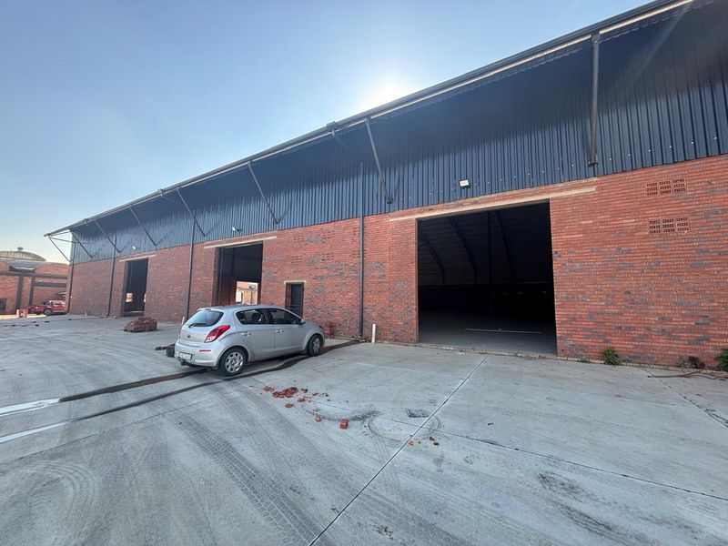 Industrial warehouse exterior featuring exposed brickwork, corrugated metal roofing, and large access openings with a spacious concrete yard area.