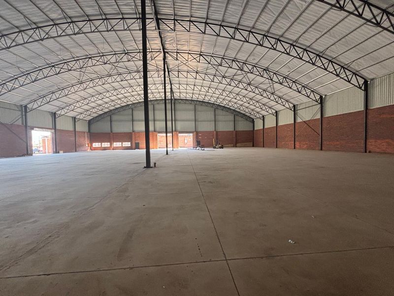 Spacious industrial warehouse featuring a high-clearance steel truss roof, durable concrete flooring, and exposed brick walls, suitable for various commercial or storage applications.