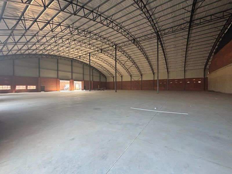Spacious industrial warehouse featuring high-clearance steel truss roofing, durable concrete flooring, and brick masonry walls, suitable for various storage or manufacturing operations.