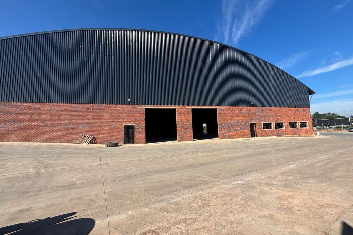 Large industrial warehouse featuring a curved corrugated metal roof, brick facade, and expansive concrete apron with multiple large access points.