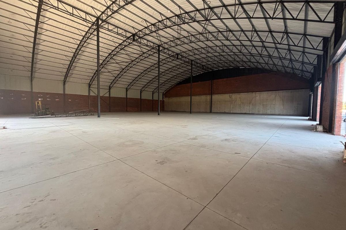 Large, open-plan industrial warehouse space featuring high-clearance steel truss roofing, durable concrete flooring, and robust brick and concrete wall construction.