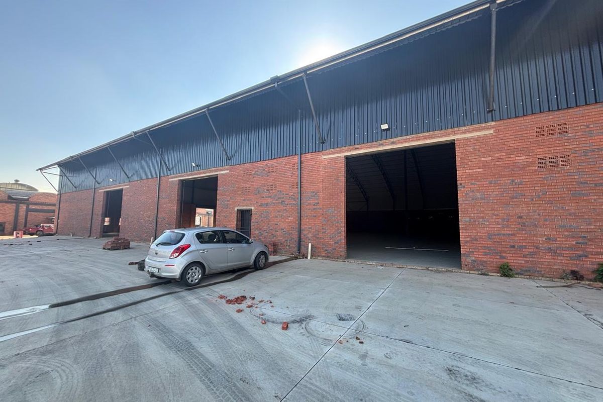 Industrial warehouse exterior featuring exposed brickwork, corrugated metal roofing, and large access openings with a spacious concrete yard area.