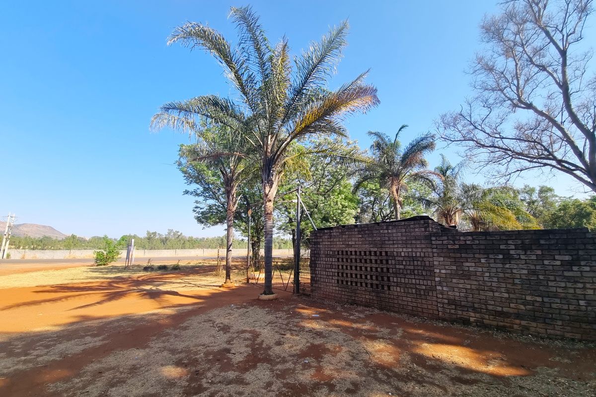 Front exterior view of the farm property featuring a brick boundary wall, metal gate, and established palm trees on a dry, open ground area.
