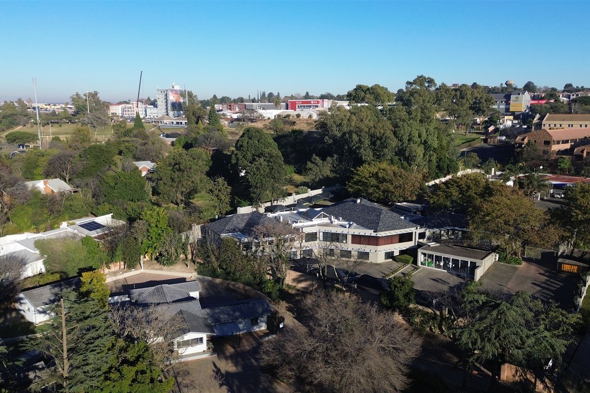 Aerial view of a commercial property complex featuring multiple buildings, paved parking areas, and established garden surroundings in a suburban setting.