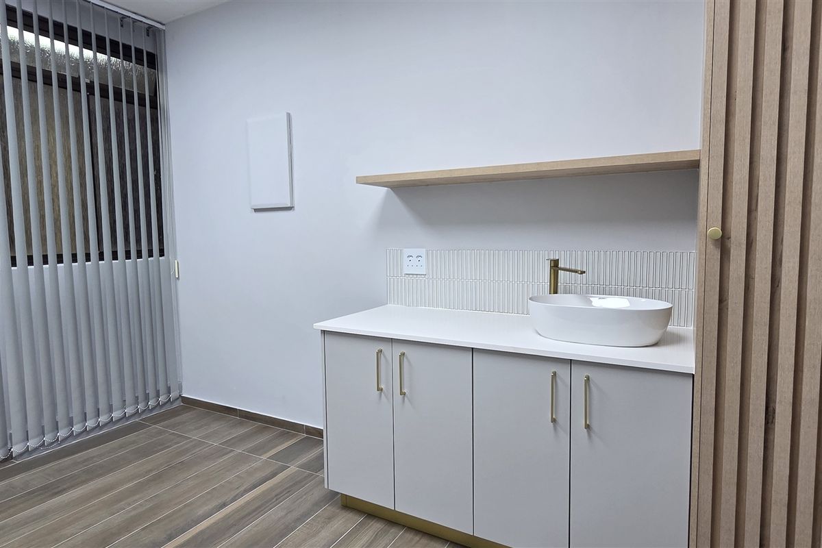 A modern kitchenette area featuring sleek cabinetry, a vessel sink with brass fixtures, tiled backsplash, and wood-look flooring.