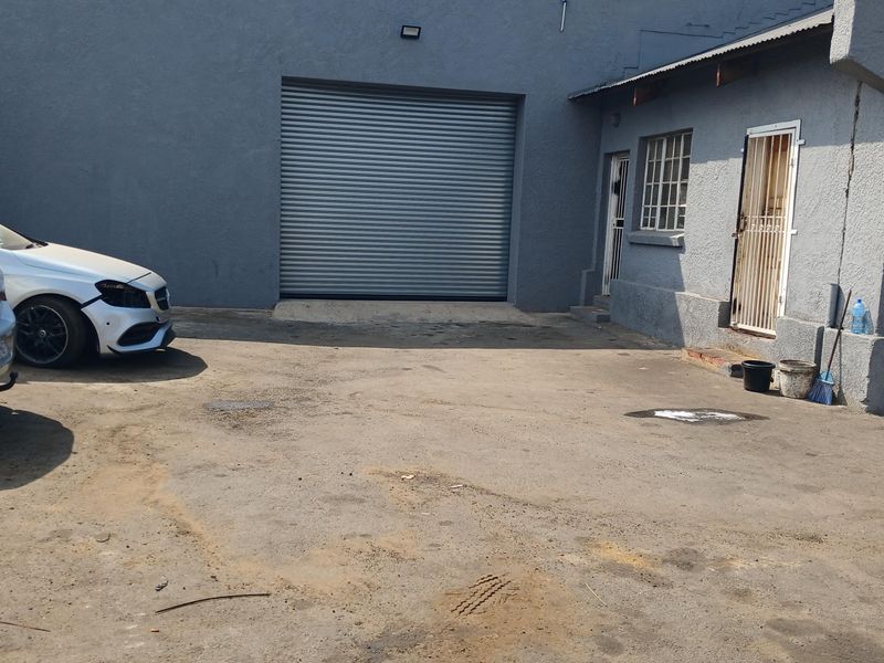Industrial rear yard featuring a large roller shutter door, security gates, and an asphalt surface, suitable for loading and access.