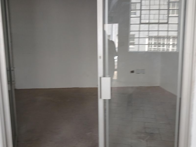 An empty industrial office space featuring concrete flooring, an aluminium framed glass door, and large industrial-style windows providing natural light.