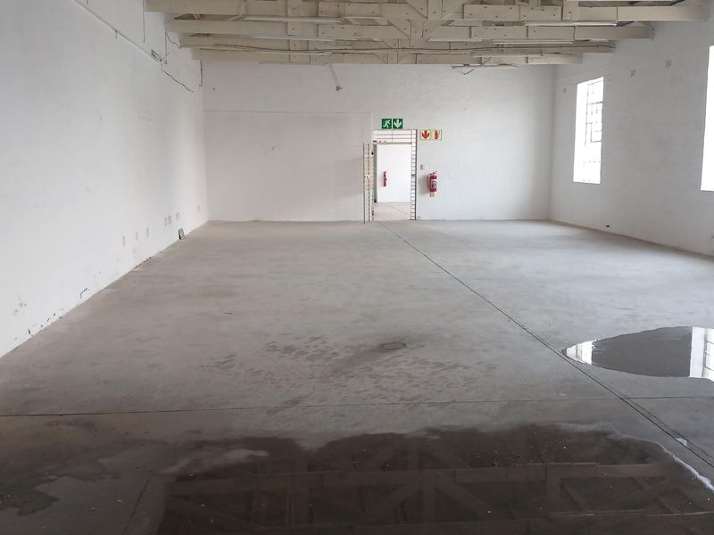 Spacious industrial utility area featuring exposed timber roof trusses, concrete flooring, and a secure access point with fire safety equipment.
