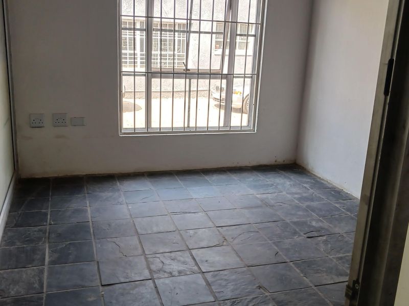 An empty office space featuring dark slate tile flooring, security bars on the window, and neutral wall finishes.