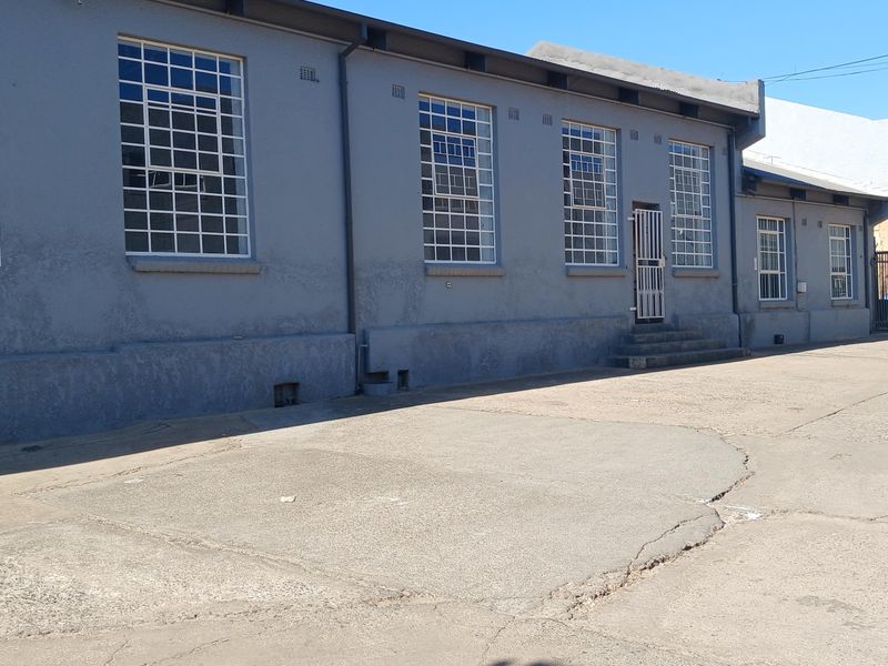Exterior view of an industrial building featuring steel-framed windows, a security entrance, and a concrete yard area with visible surface cracking.