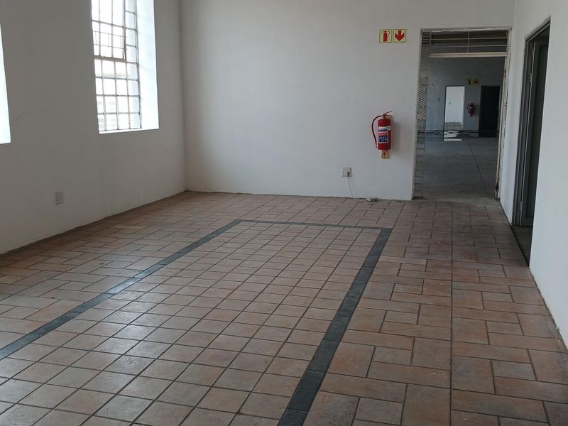 An empty, functional industrial utility space featuring durable tiled flooring, industrial-style windows, and essential fire safety equipment, offering a versatile layout for various business needs.