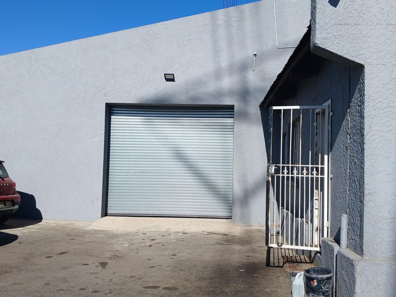 Industrial exterior featuring a large roller shutter door, security gate, and paved driveway area.