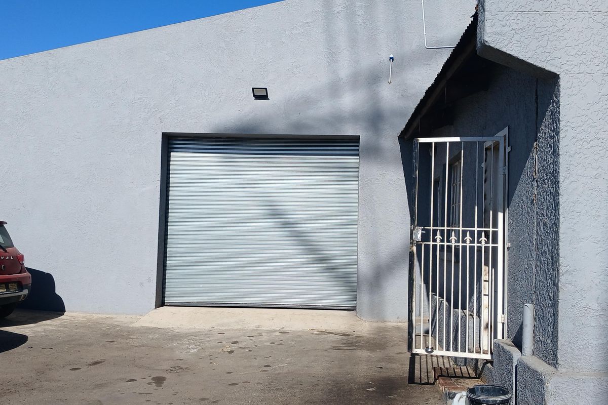 Industrial exterior featuring a large roller shutter door, security gate, and paved driveway area.