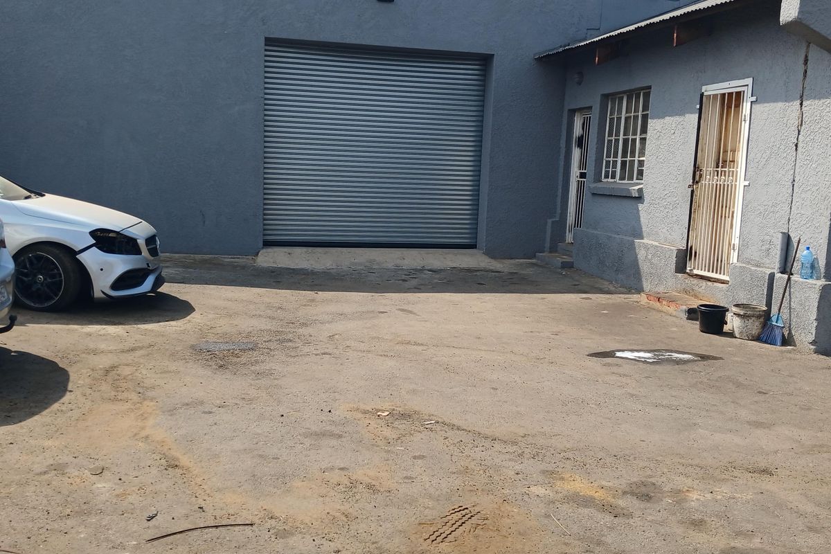 Industrial rear yard featuring a large roller shutter door, security gates, and an asphalt surface, suitable for loading and access.