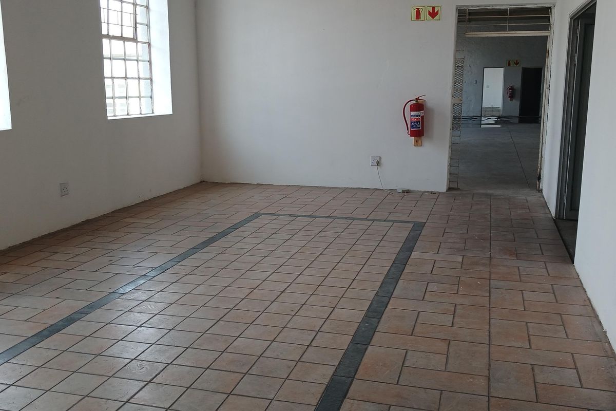 An empty, functional industrial utility space featuring durable tiled flooring, industrial-style windows, and essential fire safety equipment, offering a versatile layout for various business needs.
