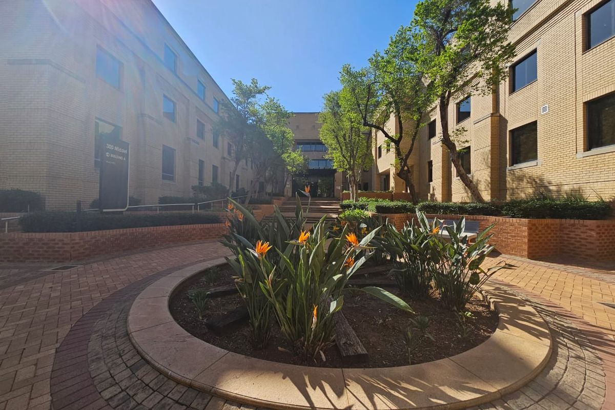 A well-maintained office complex courtyard featuring brick paving, established trees, and landscaped garden beds between the building wings.