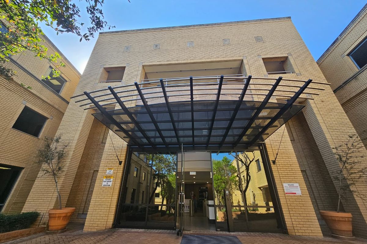 Front entrance of a professional office building featuring a modern glass canopy, brick facade, and paved access area.