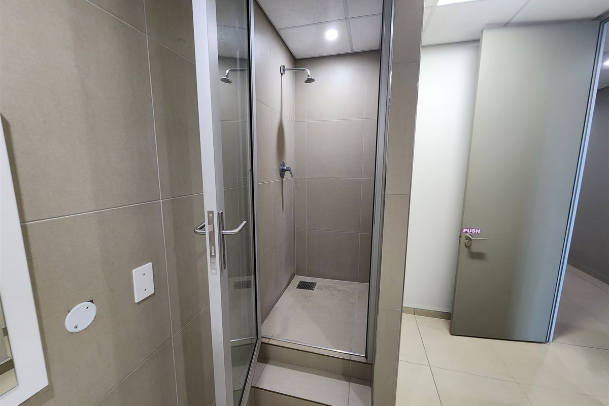 A modern office shower facility featuring neutral wall tiling, a glass door enclosure, and a raised step entry.