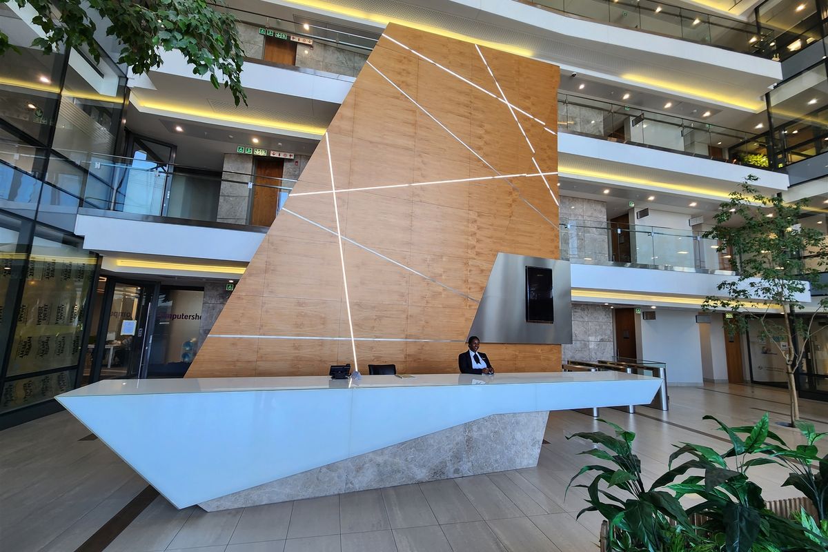 Modern office building atrium featuring a large, contemporary reception desk with integrated lighting and a striking wood-paneled feature wall.