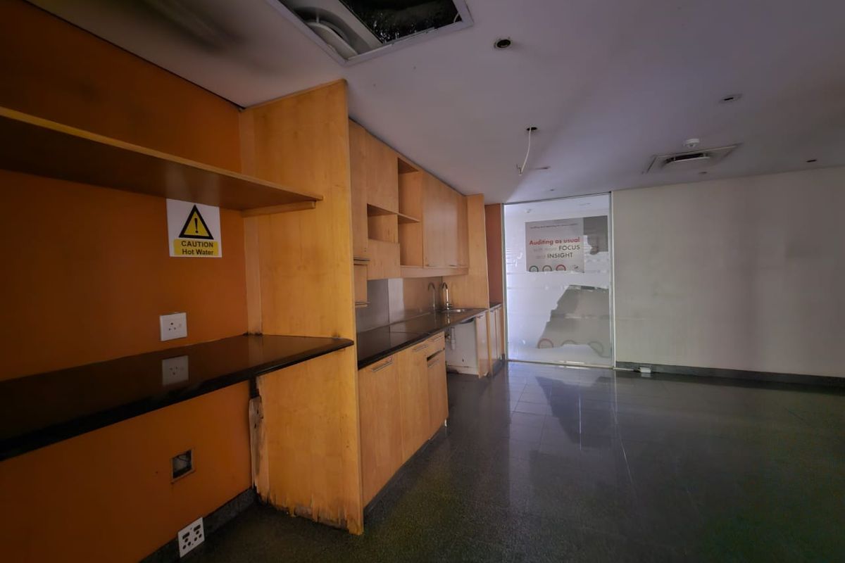 A vacant office kitchenette featuring built-in wooden cabinetry, stone countertops, and a sink, currently requiring maintenance and repairs to the ceiling and cabinetry base.