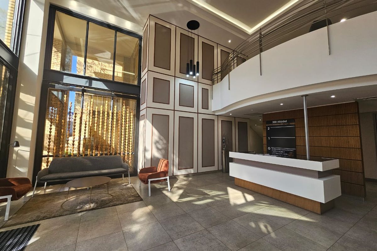 Modern double-volume office reception area featuring a sleek reception desk, tiled flooring, and expansive floor-to-ceiling windows providing ample natural light.