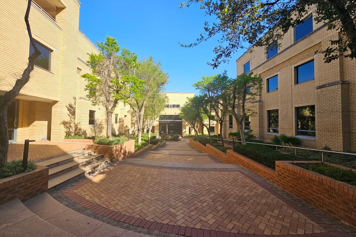 A well-maintained office complex courtyard featuring brick facade buildings, paved walkways, and established landscaping.