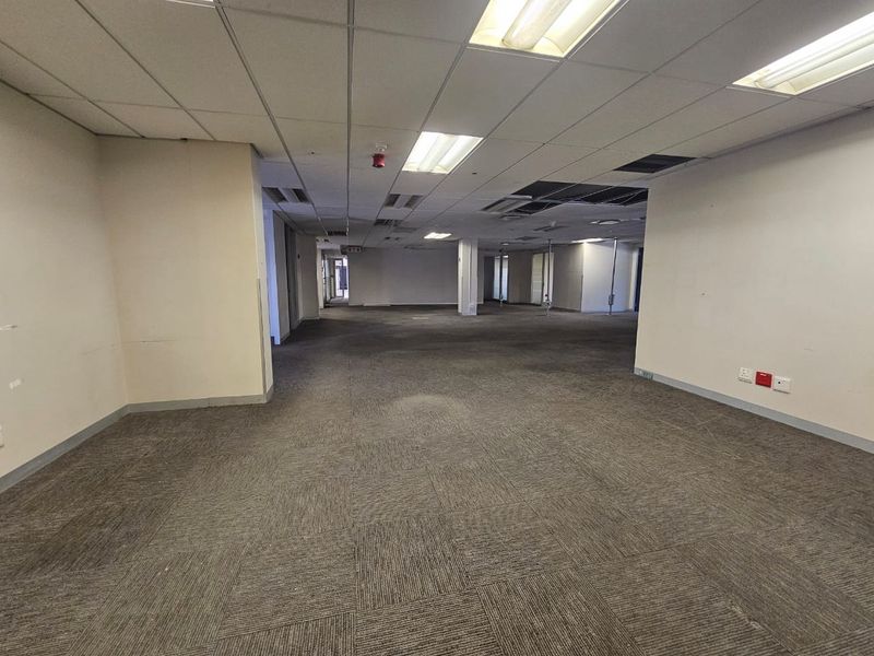 An open-plan office space featuring suspended ceilings, recessed lighting, and carpet tile flooring, currently vacant and ready for refurbishment.