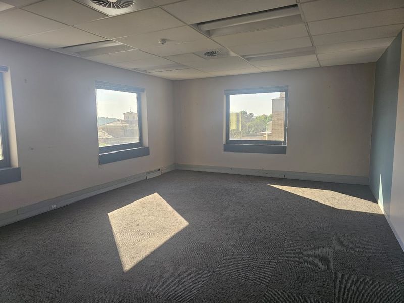 An empty, naturally lit office space featuring a suspended ceiling, recessed lighting, and carpet tile flooring.