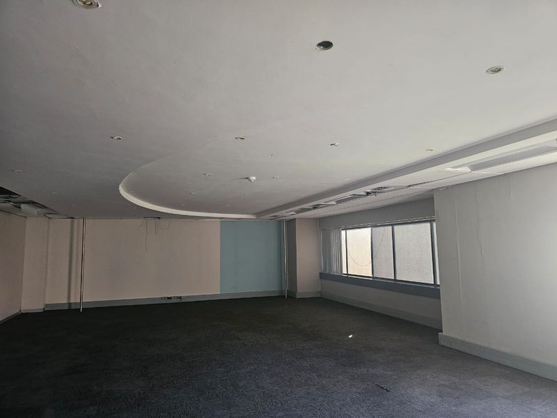 An empty, open-plan office space featuring a curved bulkhead ceiling, recessed lighting, and large windows, currently requiring maintenance and cosmetic updates.
