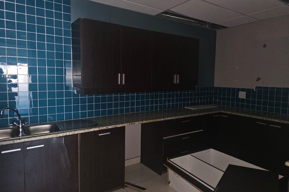 A small office kitchenette featuring dark cabinetry, granite countertops, and blue tiled backsplash, currently requiring repairs to cabinetry and ceiling finishes.