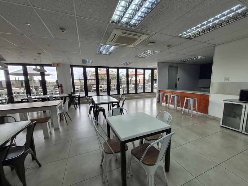 Spacious open-plan office break area featuring tiled floors, suspended ceilings with integrated lighting, and large bi-fold doors leading to an outdoor patio.