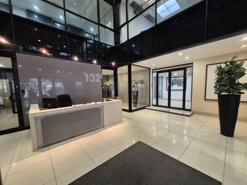 Modern office building entrance lobby featuring a reception desk, high ceilings, glass partitioning, and polished tiled flooring.
