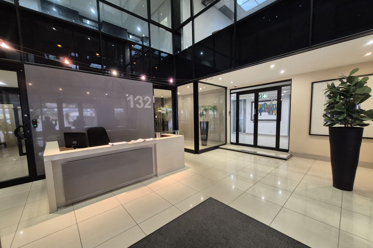 Modern office building entrance lobby featuring a reception desk, high ceilings, glass partitioning, and polished tiled flooring.