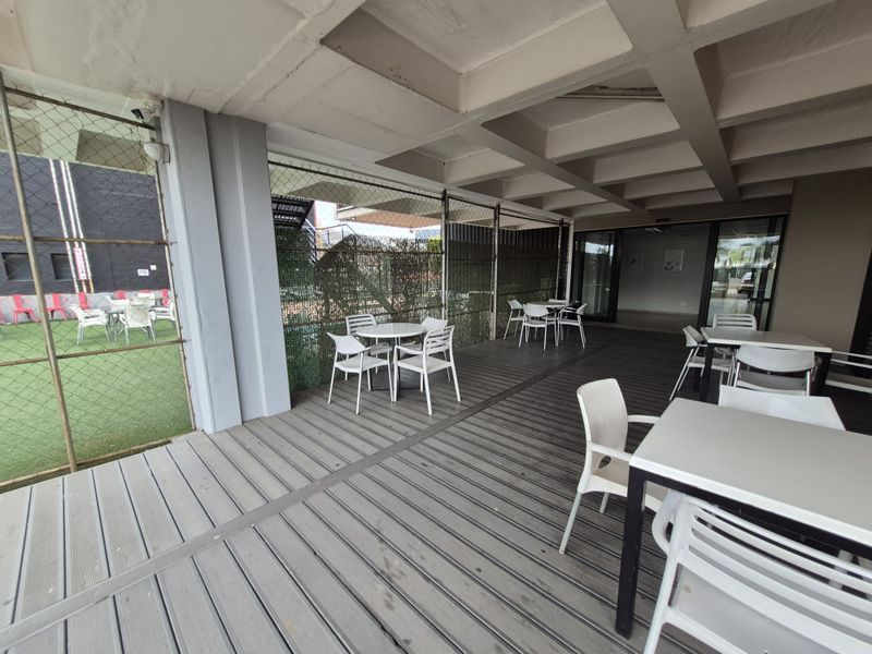 Covered outdoor patio area featuring durable decking, exposed concrete ceiling beams, and secure perimeter fencing, suitable for office break-out or social space.