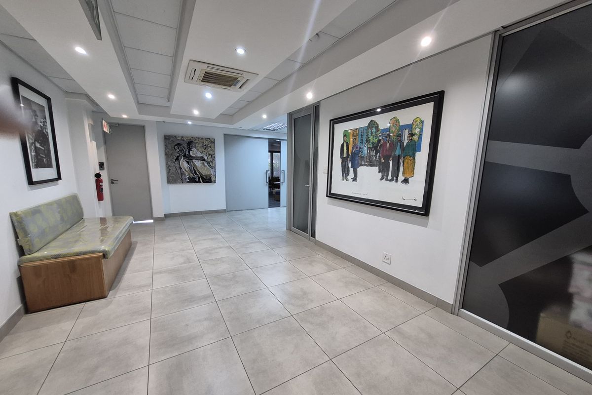 A modern office hallway featuring tiled flooring, recessed ceiling lighting, a ducted air conditioning unit, and glass partition doors.