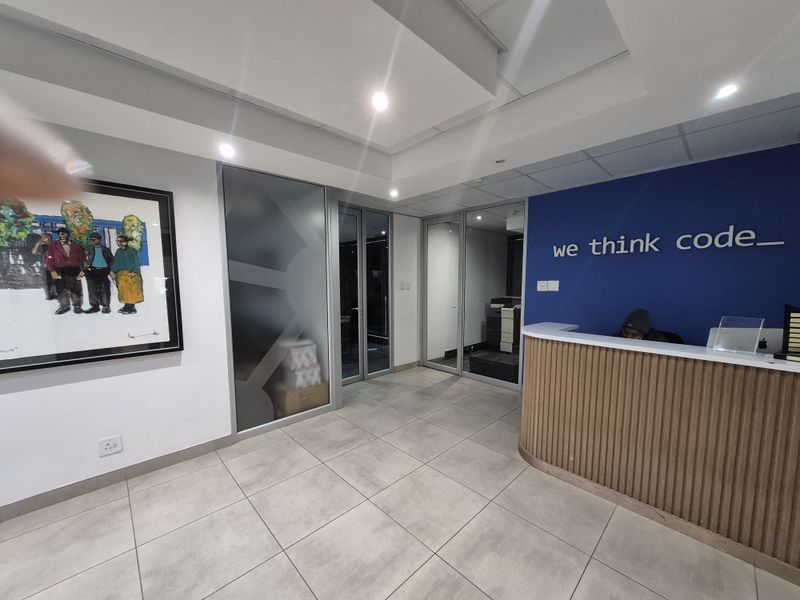 Modern office reception area featuring a curved wooden desk, glass partitions, and professional recessed lighting.