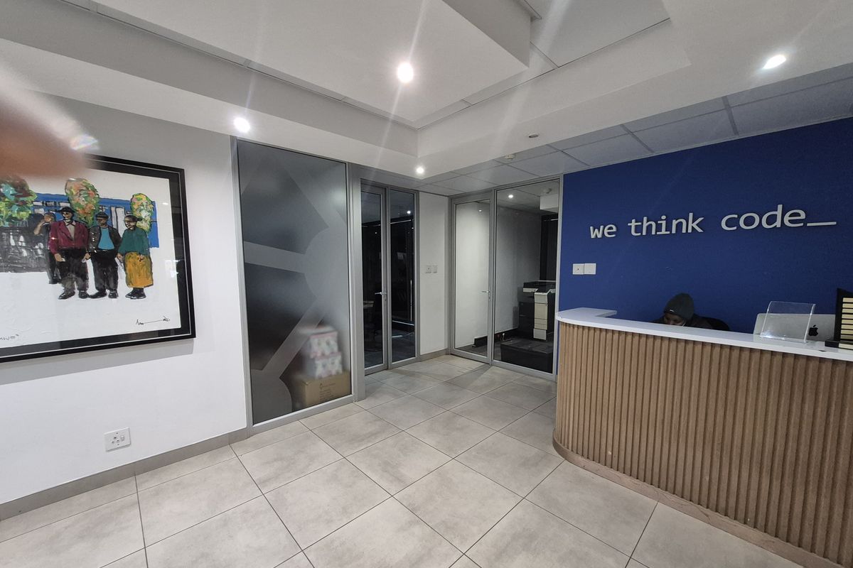 Modern office reception area featuring a curved wooden desk, glass partitions, and professional recessed lighting.