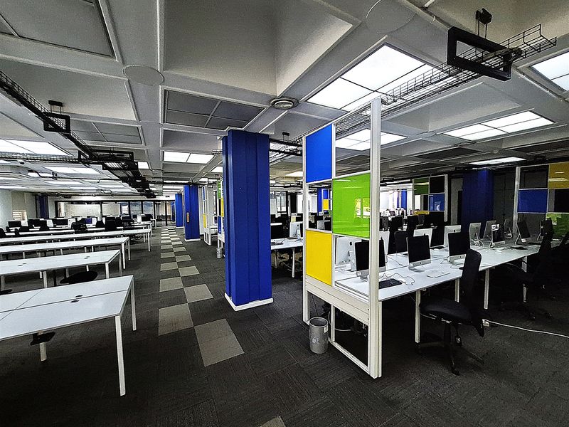 Open-plan office space featuring a suspended ceiling with recessed lighting, exposed cable management, and integrated desk partitions with a carpeted floor.
