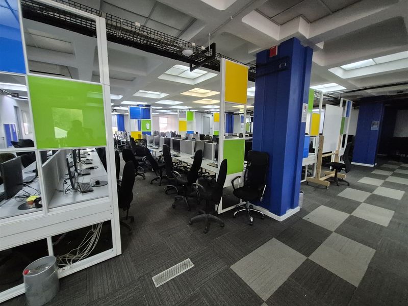 Open-plan office space featuring modular workstations, colorful partition screens, suspended ceiling grid, and carpeted flooring with integrated cable management systems.