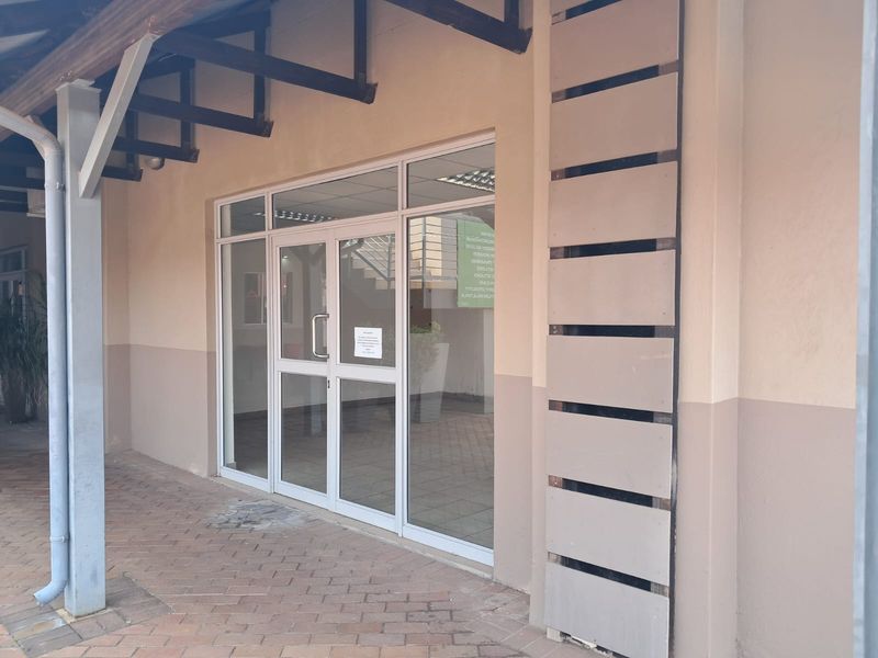 A clean office entrance featuring an aluminium-framed glass door, paved walkway, and covered porch area with decorative wall detailing.