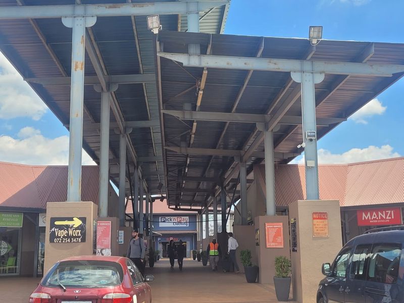 A covered outdoor walkway entrance to a commercial office and retail complex featuring a steel roof structure and paved pedestrian access.