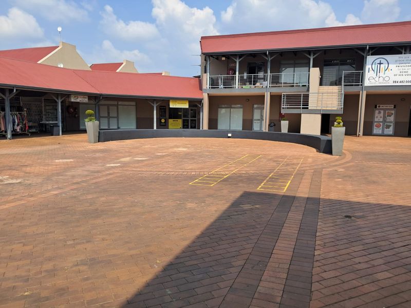 A paved courtyard area within a commercial office complex, featuring multi-level office units with metal roofing and external stair access.