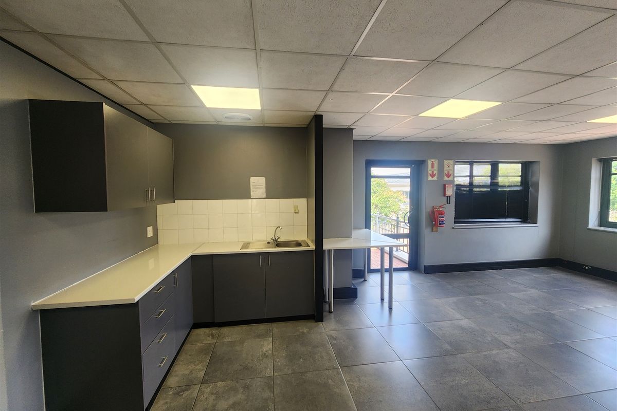 A functional office kitchenette area featuring dark grey cabinetry, white countertops, a stainless steel sink, and tiled flooring with a suspended ceiling.