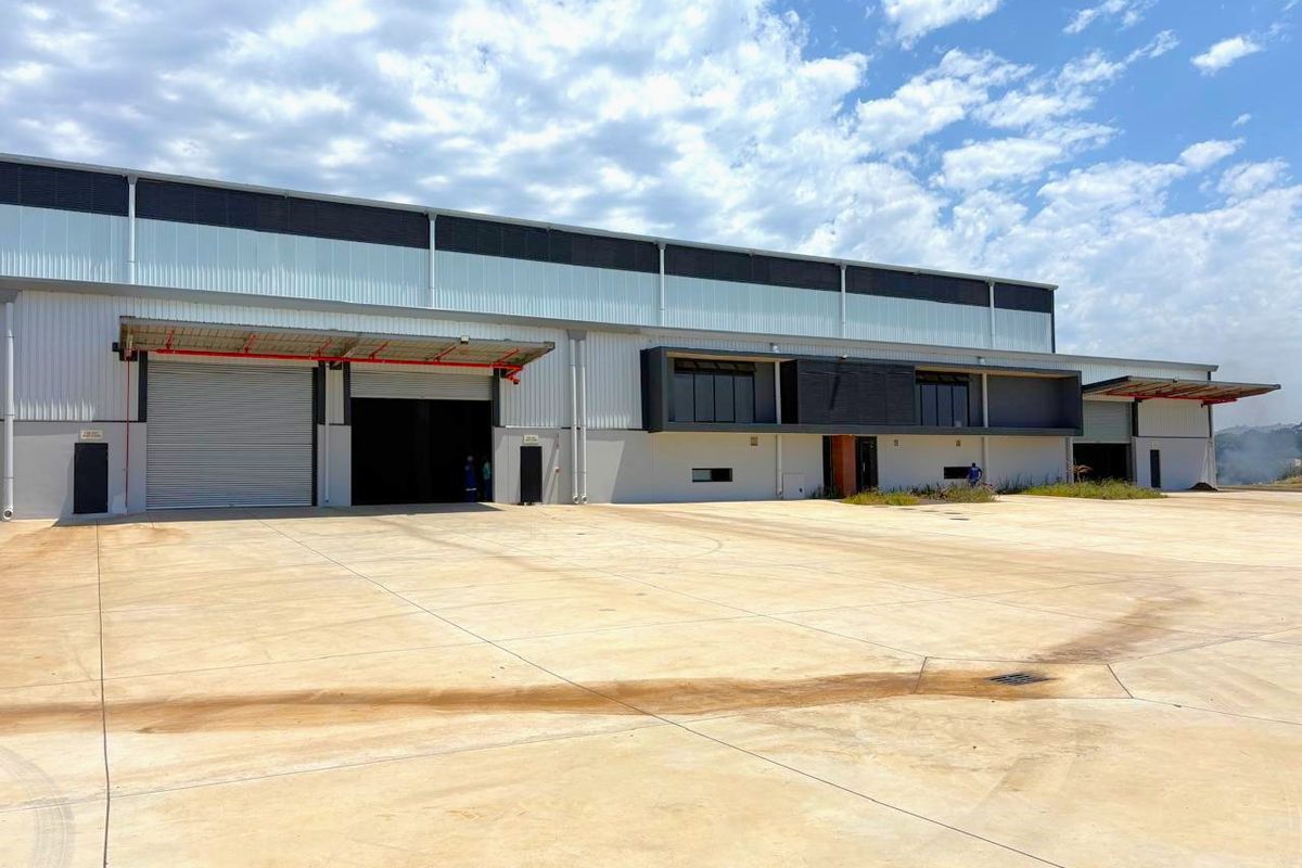 A modern industrial warehouse facility featuring large roller shutter doors, loading bays, and a spacious concrete yard area.