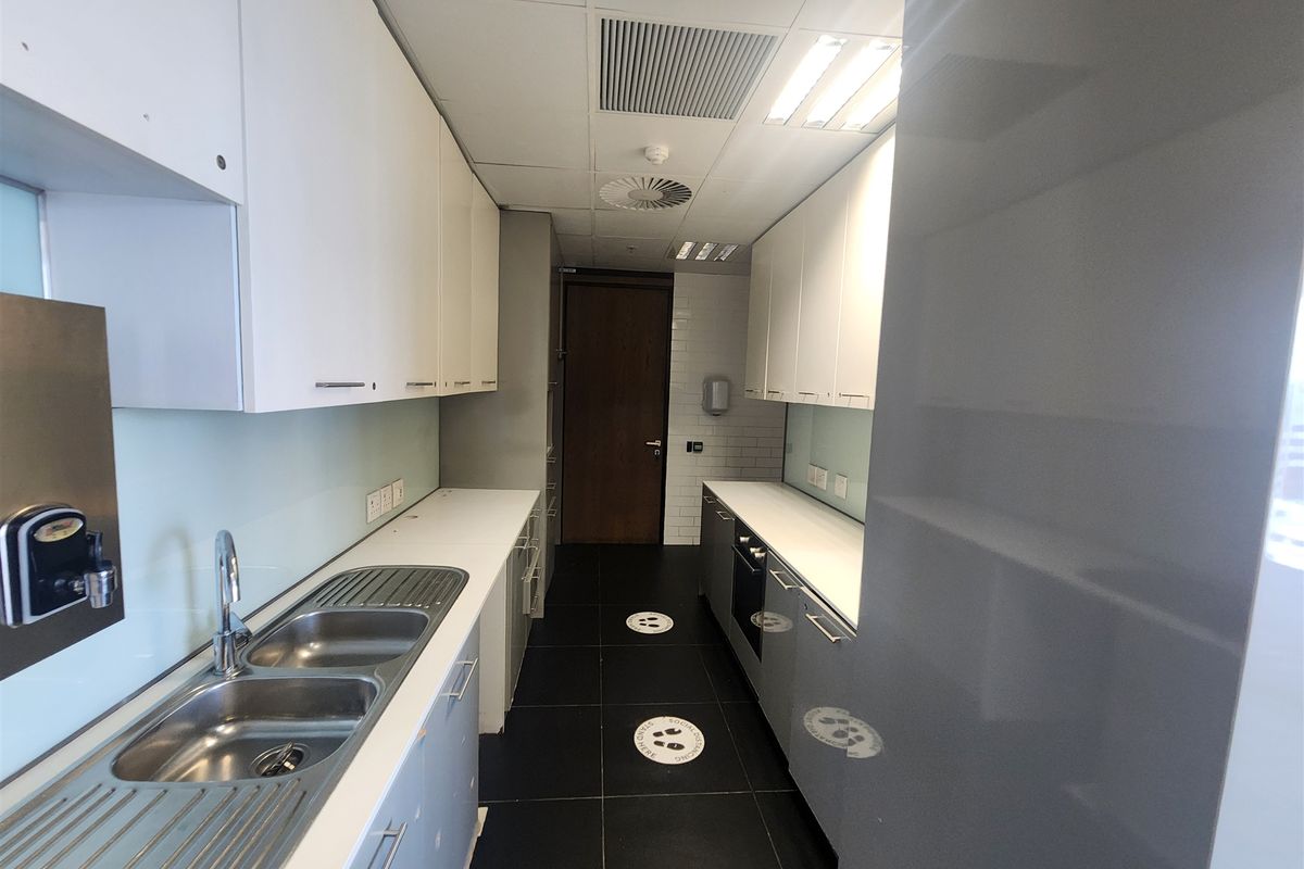 A functional office kitchenette featuring white cabinetry, a double stainless steel sink, integrated oven, and modern tiled flooring.