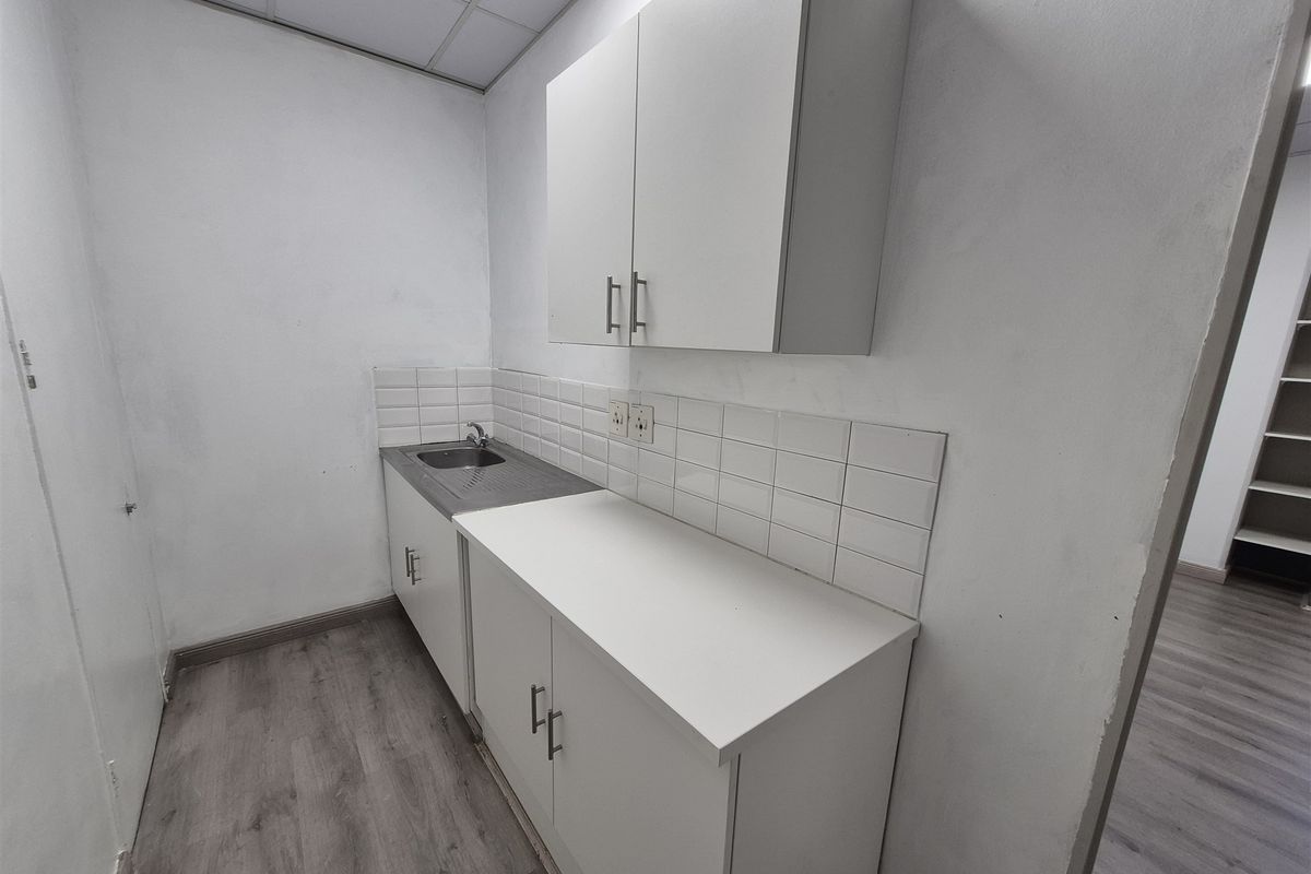 A compact office kitchenette featuring white cabinetry, a stainless steel sink, tiled backsplash, and durable wood-look flooring.
