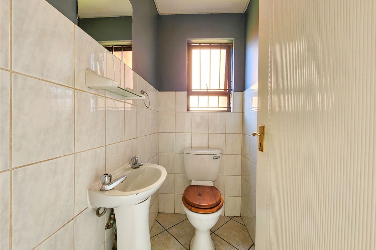 A compact office restroom featuring a pedestal basin, a standard toilet, and tiled walls with a window for natural light.