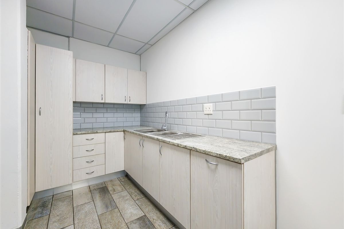 A functional office kitchenette featuring light wood-grain cabinetry, granite countertops, a stainless steel sink, and modern subway tile backsplash.